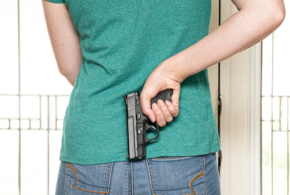 woman with handgun behind back at door