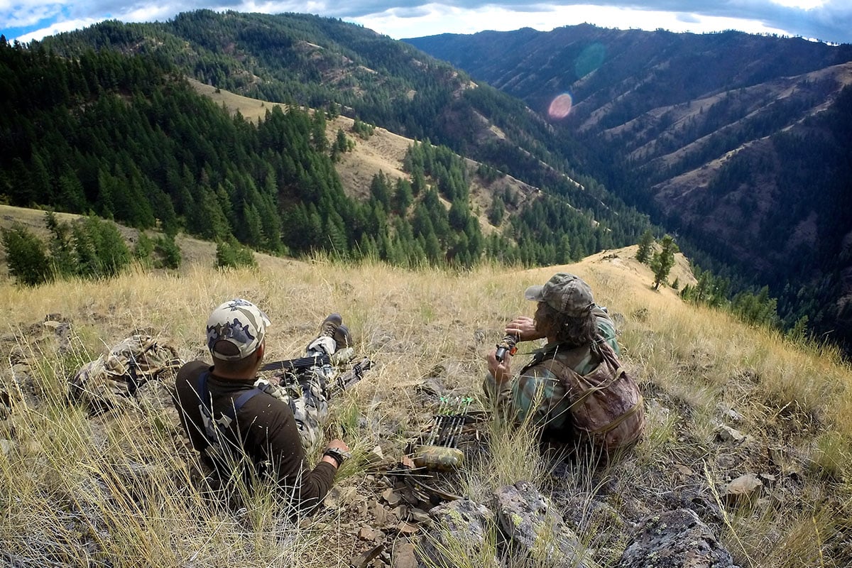 Two men sitting on a mountian top, locating elk