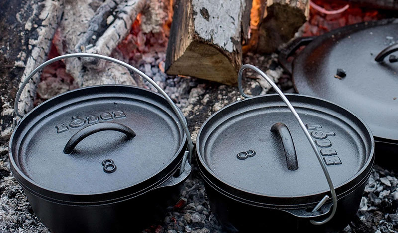Lodge cast iron Dutch ovens with legs on coals over a campfire