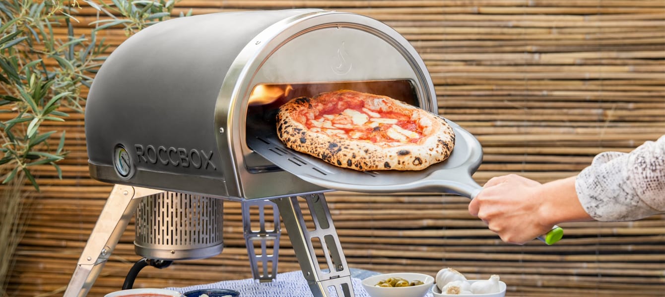 Person pulling pizza from a Gozney pizza oven
